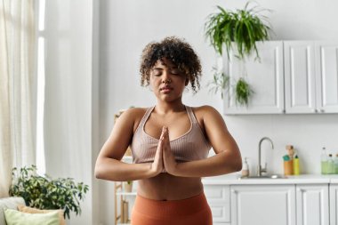 Genç bir kadın evde meditasyon yaparken bir anlık huzurun tadını çıkarır..