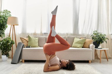 A young woman performs yoga while relaxing in her home. clipart