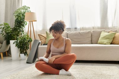 A young woman relaxes on the floor, smiling while stretching at home. clipart