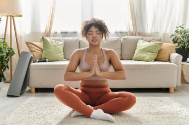 Genç bir kadın rahat bir yaşam alanında meditasyon yapıyor..