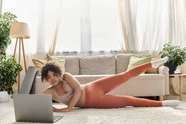 Bir kadın laptopunu kullanırken yerde spor yapıyor..
