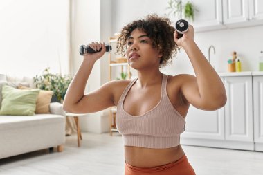 Güzel bir Afrikalı Amerikalı kadın evde çalışırken ağırlık kaldırıyor..