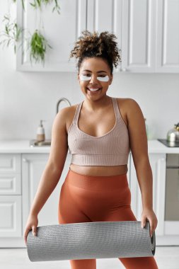 Evde yoga minderini açarken genç bir kadın ışıl ışıl gülümsüyor..
