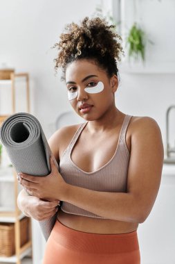 Kendine iyi bakan bir kadın, yoga minderini rahatlatıcı bir maskeyle tutar..
