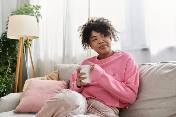 stock image A young woman sips her drink while enjoying a peaceful moment at home.