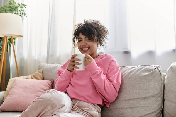 Улыбающаяся молодая женщина расслабляется на диване, потягивая кофе в теплой, уютной атмосфере.