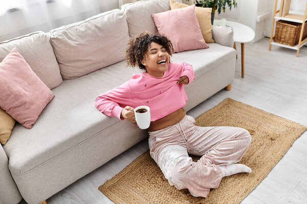 Молодая женщина смеется, потягивая кофе в удобной гостиной.