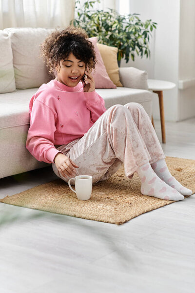 Молодая женщина улыбается, разговаривая по телефону и наслаждаясь чаем дома.