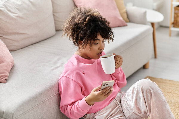 Потягивая кофе и прокручивая, молодая женщина расслабляется в своем комфортном жизненном пространстве.