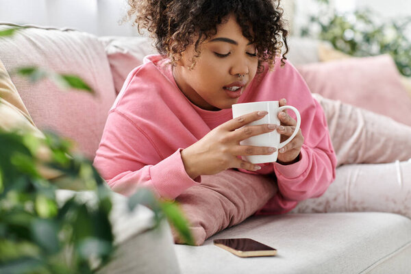 A young woman enjoys a warm beverage while lounging on a comfy couch.