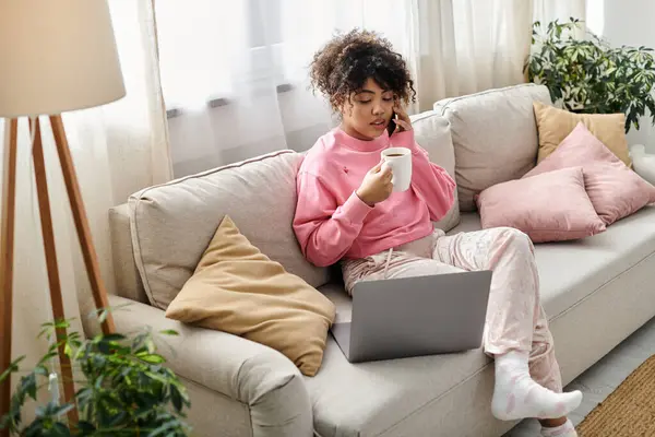 stock image A young woman enjoys her cozy time at home, sipping tea while on the phone.