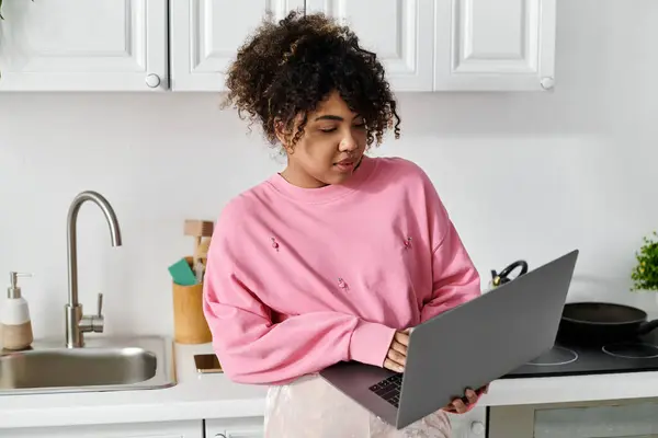 stock image She engages thoughtfully with her laptop in a warm, inviting kitchen.