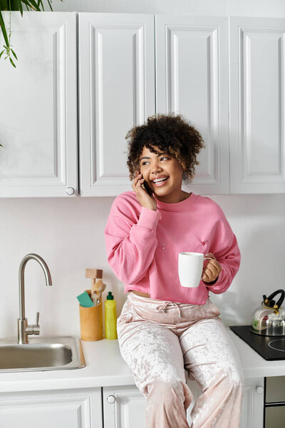 Женщина расслабляется на кухонном столе, держа горячую чашку во время чата.