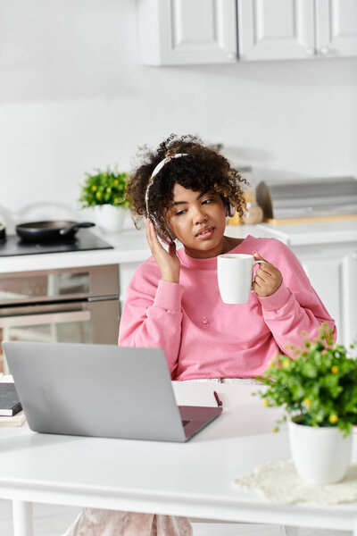 A young woman enjoys a cozy moment at home with coffee and her laptop.