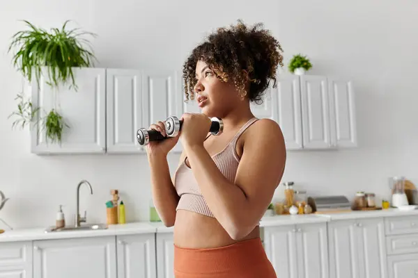 stock image A young woman lifts weights while enjoying her time at home.