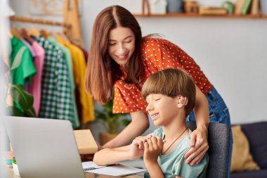 A mother lovingly engages with her hearing impaired son while he studies. clipart