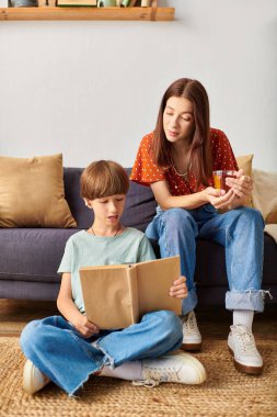 Bir anne sıcak bir içeceğin tadını çıkarırken oğluna kitap okutur..