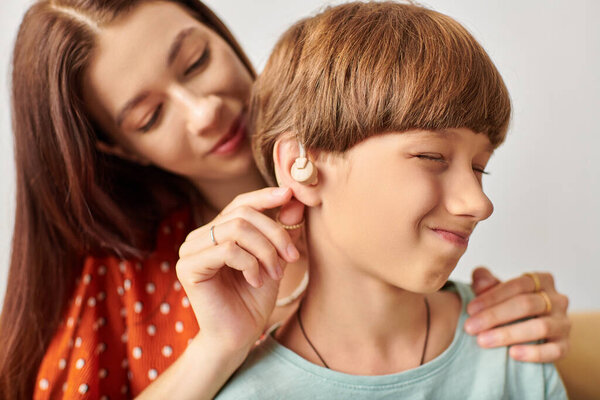 A mother lovingly assists her hearing impaired son with his hearing device.