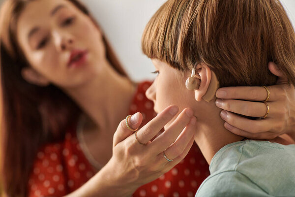 A mother gently assists her son with his hearing aid, sharing a tender moment together.