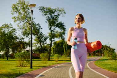 Genç bir kadın açık hava yoga seansına hazır bir şekilde parkta dolaşıyor..