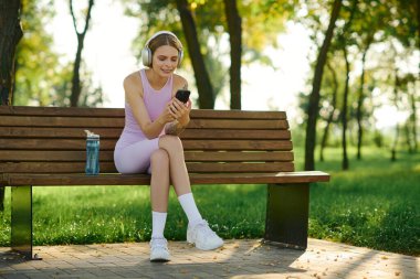 Genç bir kadın bankta otururken müzik dinliyor..