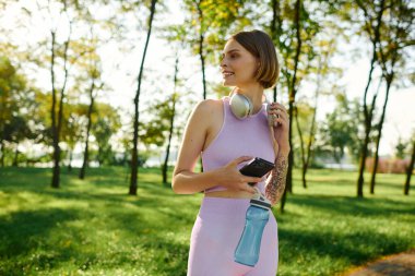 Canlı yeşil bir parkta müzik dinlerken genç bir kadın gülümsüyor..