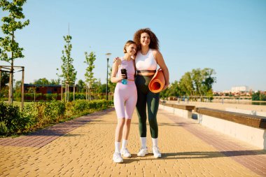 İki kadın parkta yogaya hazırlanırken sıcak bir anı paylaşıyor..