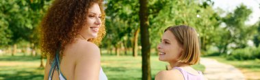 Two women share laughter and love under the trees in a vibrant green space. clipart