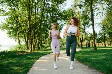 Two women enjoy jogging side by side in a vibrant green park. clipart