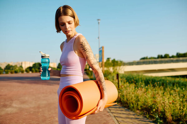 Женщина наслаждается солнечным днем, готовая к йоге в парке с ковриком и водой.