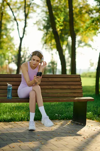 Stock image A young woman relaxes on a bench, absorbed in her music.