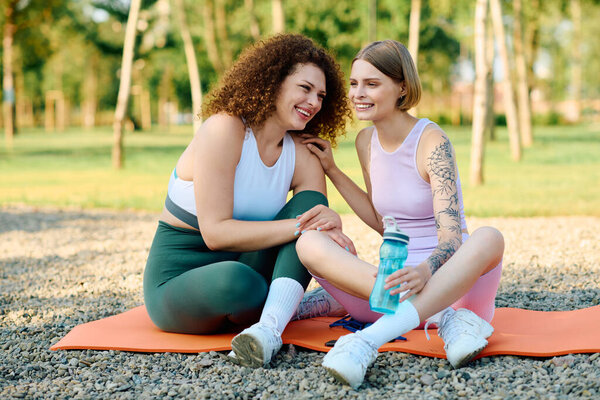 A joyful couple sits on a mat, laughing and sipping water while enjoying their day outdoors.