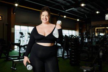 Geniş bedenli bir kadın, canlı bir spor salonunda vücut pozitifliğini desteklemek için kendine güvenerek spor yapıyor..