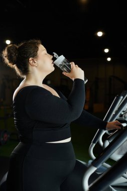 Kendine güvenen genç bir kadın, etkili spor salonunda ferahlatıcı bir yudum su alır..