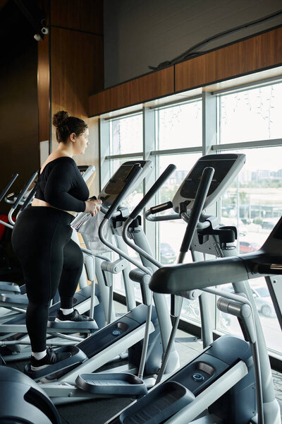 Молодая женщина с большим размером уверенно тренируется на эллиптическом эллипсе, принимая ее фитнес-путешествие.