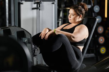 Genç bir kadın hareketli bir spor salonunda aktif giysi, kuvvet ve vücut pozitifliği ile egzersiz yapıyor..