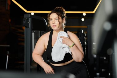 Geniş bedenli genç bir kadın spor salonunda özgüvenle egzersiz yapıyor. Güç ve vücut pozitifliği gösteriyor..
