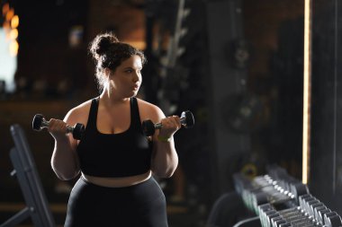 Geniş bedenli bir kadın halterleri rahatça kaldırır. Enerjik bir spor salonunda güç ve sağlığını kutlar..