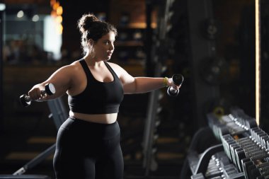 Büyük beden bir kadın, spor salonunda ağırlık kaldırır. Vücut pozitifliği ve dayanıklılığını somutlaştırır..