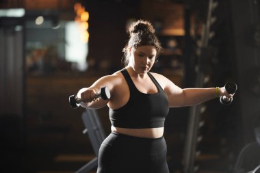 Kararlı genç bir kadın spor salonunda ağırlık kaldırıyor, dayanıklılığını ve vücut pozitifliğini kutluyor..