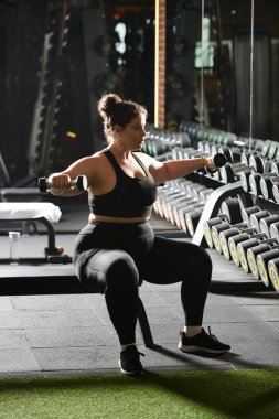 Geniş beden bir kadın spor salonunda halterlerle egzersiz yapıyor, özgüven ve zindelik timsali..