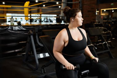 Büyük beden bir kadın spor salonunda halterlerle rahatça egzersiz yapıyor..
