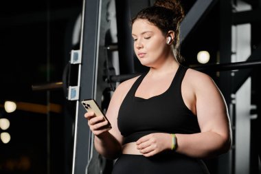 Aktif giyinen genç bir kadın spor salonunda spor yaparken telefonuyla aktif olarak meşgul oluyor..
