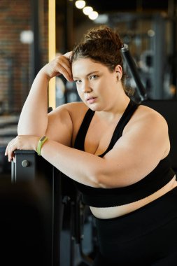 Hareketli bir spor salonunda kendine güveni olan genç bir kadın ara verir ve vücut pozitifliğini gösterir..