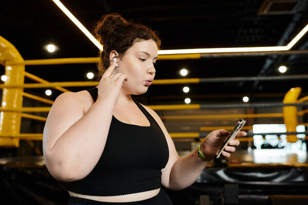 Женщина plus-size наслаждается тренировками, слушая музыку и проверяя сообщения в спортзале.