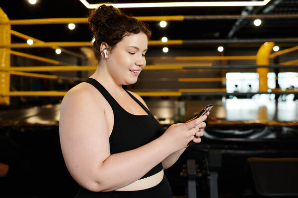Женщина plus-size наслаждается своей рутиной тренировок, занимаясь со своим телефоном в оживленной атмосфере спортзала.