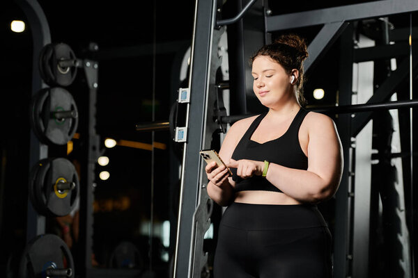 Уверенная в себе молодая женщина проверяет свой телефон, обнимая тело позитивной тренировкой в активной одежде.