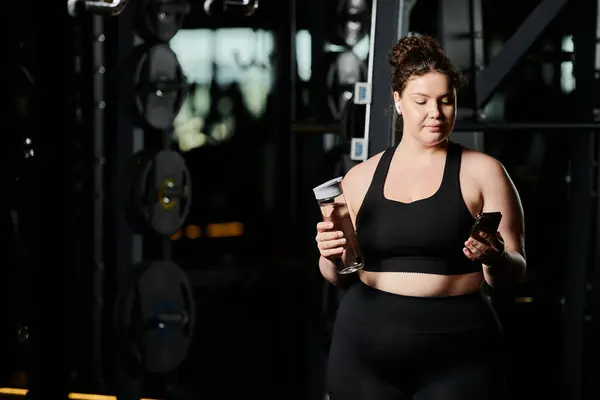 stock image A confident young woman engages in her fitness journey, checking her phone in a lively gym environment.