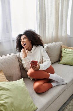 A young woman laughs while lounging comfortably in her cozy living room. clipart