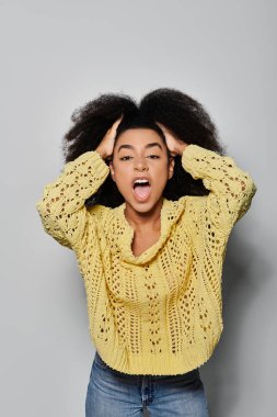 A young woman in a yellow sweater exuberantly showcases her lively personality against a grey backdrop. clipart